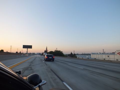 2003 Ford Crown Victoria - Empty-looking twilight freeway with one dark sedan, roadside billboard and industrial buildings.