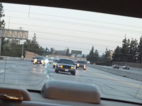 2003 Ford Crown Victoria - Black Crown Victoria-style sedan leads traffic at twilight, viewed through the windshield.