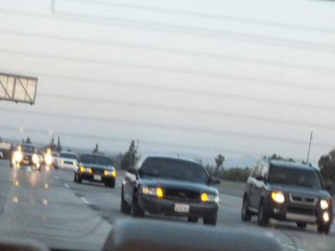 2003 Ford Crown Victoria - Headlights on at twilight as a dark sedan and boxy SUV travel a multilane freeway.