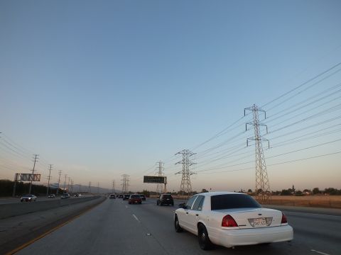2003 Ford Crown Victoria - White full-size sedan rides the right lane at twilight as power pylons march along the shoulder.