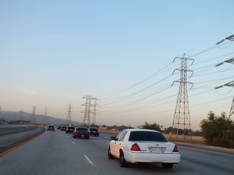 2003 Ford Crown Victoria - Twilight freeway behind a white sedan, steel transmission towers and wires filling the right side.