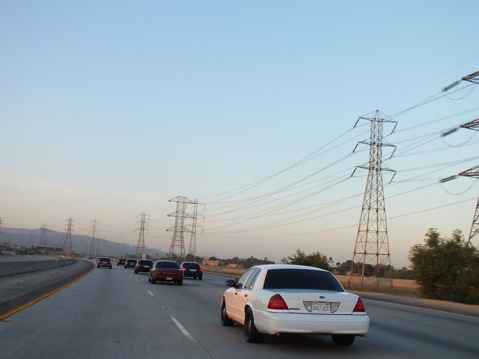 Rear of white Ford Crown Victoria on freeway at dusk with transmission towers at right