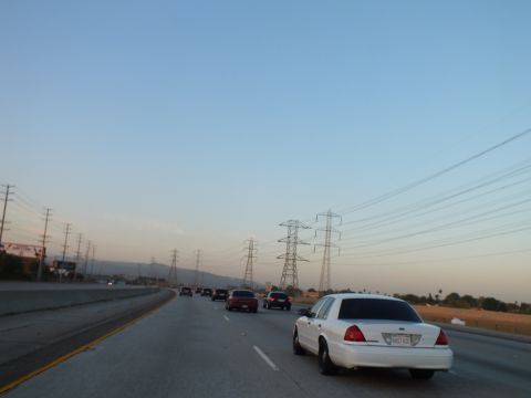 2003 Ford Crown Victoria - White full-size sedan and a red car on a twilight freeway lined by electrical towers.