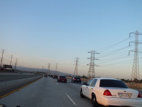 2003 Ford Crown Victoria - White sedan in the right lane at twilight with high-voltage pylons and scrubland alongside.