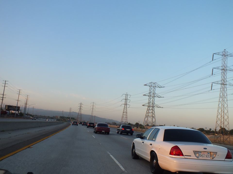 White Ford Crown Victoria on freeway at dusk, transmission towers and dry brush at right