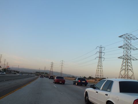 2003 Ford Crown Victoria - Twilight freeway traffic including a white sedan and red SUV beside multiple power pylons.