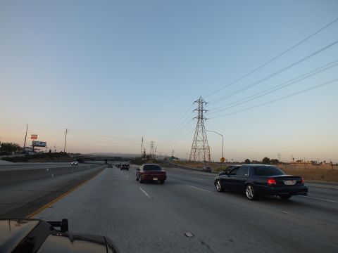2003 Ford Crown Victoria - Twilight freeway with a dark sedan trailing a maroon car, a lone pylon against the sky.