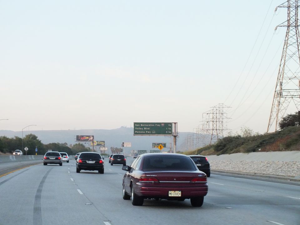 Maroon sedan on freeway at dusk below green overhead sign for San Bernardino Fwy and Valley Blvd