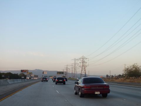 2003 Ford Crown Victoria - Dark red sedan on a twilight freeway, electrical pylons at right and lit billboards in the distance.