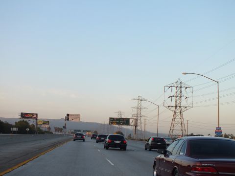 2003 Ford Crown Victoria - Dark red sedan travels the right lane at twilight beside a high streetlight and power pylons.