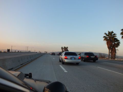 2003 Ford Crown Victoria - Two sedans cruise a concrete freeway near palm trees as the sky fades to dusk.