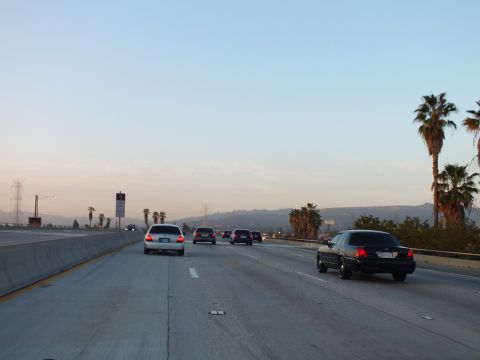 2003 Ford Crown Victoria - Freeway traffic spreads across empty lanes with palm trees lining the right shoulder.