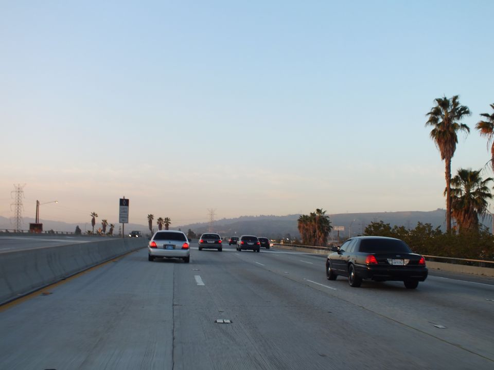 Black full-size sedan and silver wagon on a wide freeway with palms at sunset