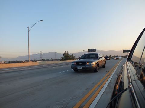 2003 Ford Crown Victoria - dark full-size sedan changes lanes on the freeway as mountains rise in the haze.