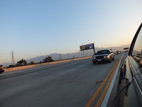 2003 Ford Crown Victoria - sedan rolls along the freeway past a lit billboard showing the number 70.