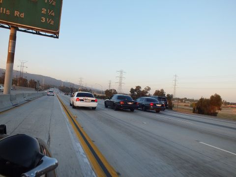 2003 Ford Crown Victoria - white sedan leads two black sedans under a green highway sign marked Rd 2 1/2.