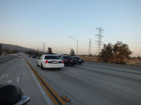 2003 Ford Crown Victoria - white sedan flanks black sedans on the freeway beneath a large transmission tower.