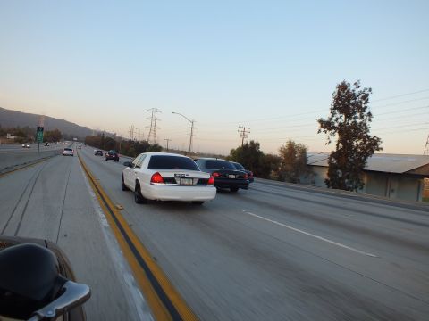 2003 Ford Crown Victoria - white full-size sedan rides beside a black sedan on a wide concrete freeway.