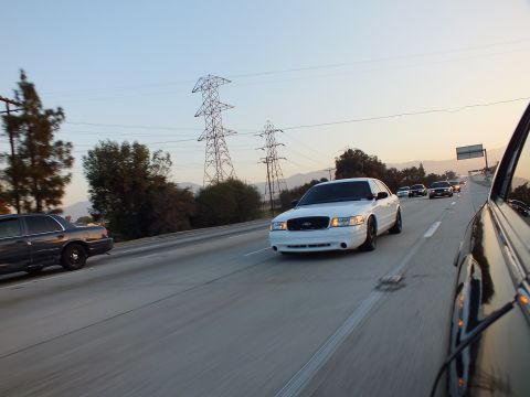 2003 Ford Crown Victoria - white full-size sedan approaches in the freeway lane near tall power towers.