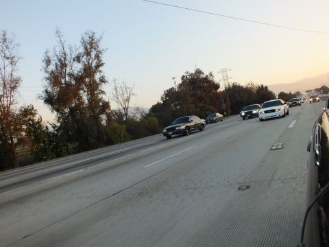 2003 Ford Crown Victoria - cluster of sedans heads down the freeway toward distant hills in the evening haze.