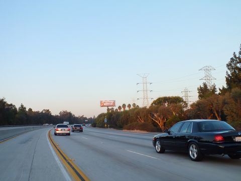 2003 Ford Crown Victoria - black sedan cruises the freeway past power towers and a small roadside billboard.