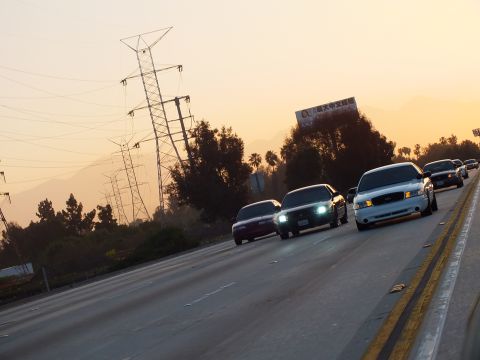 2003 Ford Crown Victoria - convoy of cars with headlights on streams down the freeway into the golden sunset.