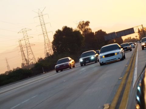 2003 Ford Crown Victoria - Sedans run in formation down the freeway with headlights glowing at golden hour.