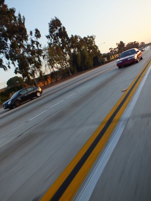 2003 Ford Crown Victoria - black hatchback and maroon sedan travel the freeway along a bold double yellow line.