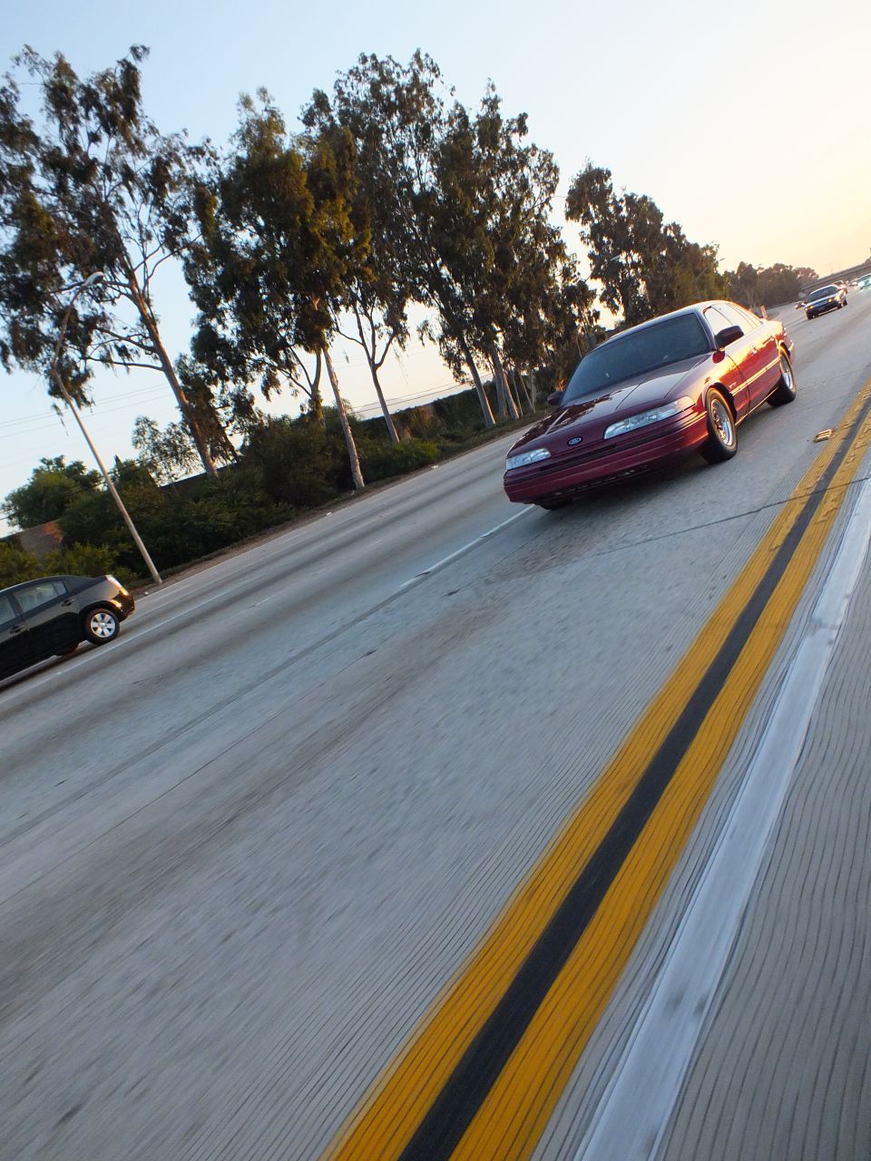 Maroon Ford Taurus sedan on freeway beside double yellow line at dusk