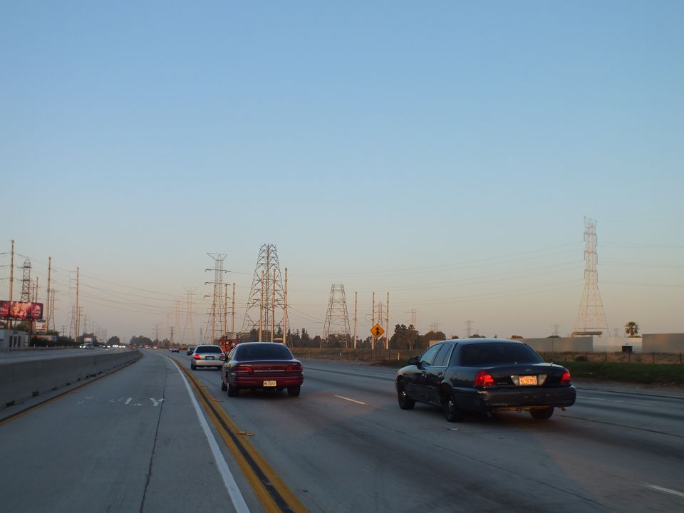 Dark sedan and maroon coupe on multi-lane freeway at dusk with power line towers