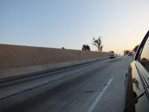 2003 Ford Crown Victoria - Open highway alongside a masonry noise barrier, sparse traffic ahead at sunset.