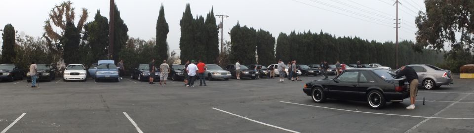 Panorama of car meet with black coupe at right and rows of sedans across foggy lot