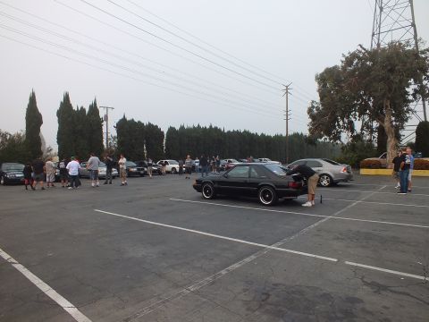 2003 Ford Crown Victoria - dark coupe sits with its trunk open while a group gathers across the gray lot.
