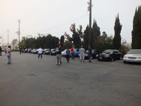 2003 Ford Crown Victoria - Wide view of a car meet with attendees and parked sedans on a foggy gray morning.