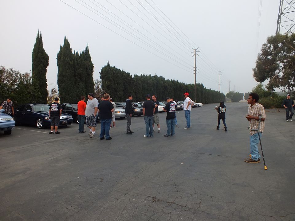 Attendees talking in foggy lot beside parked cars with man on crutches at right