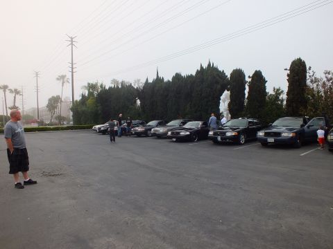 2003 Ford Crown Victoria - Dark and silver Panther-platform sedans parked diagonally as attendees gather under overhead wires.