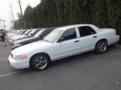2003 Ford Crown Victoria - Lowered white Crown Victoria shown front-three-quarter beside a row of other parked sedans.