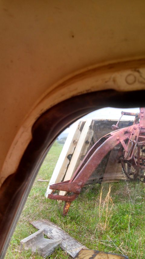 1979 Ford Bronco - View from inside a vehicle shows a rusty loader attachment mounted on a trailer in a grassy field.