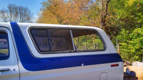 1979 Ford Bronco - The side of a 1979 Ford Bronco with a white and blue camper shell is visible.