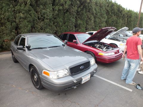 2003 Ford Crown Victoria - Gray Crown Victoria with steel-look wheels in the foreground; a maroon hood-up car sits beside it.