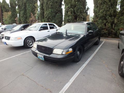 2003 Ford Crown Victoria - Black Crown Victoria sits low on dark steel wheels, a white example parked to its left.