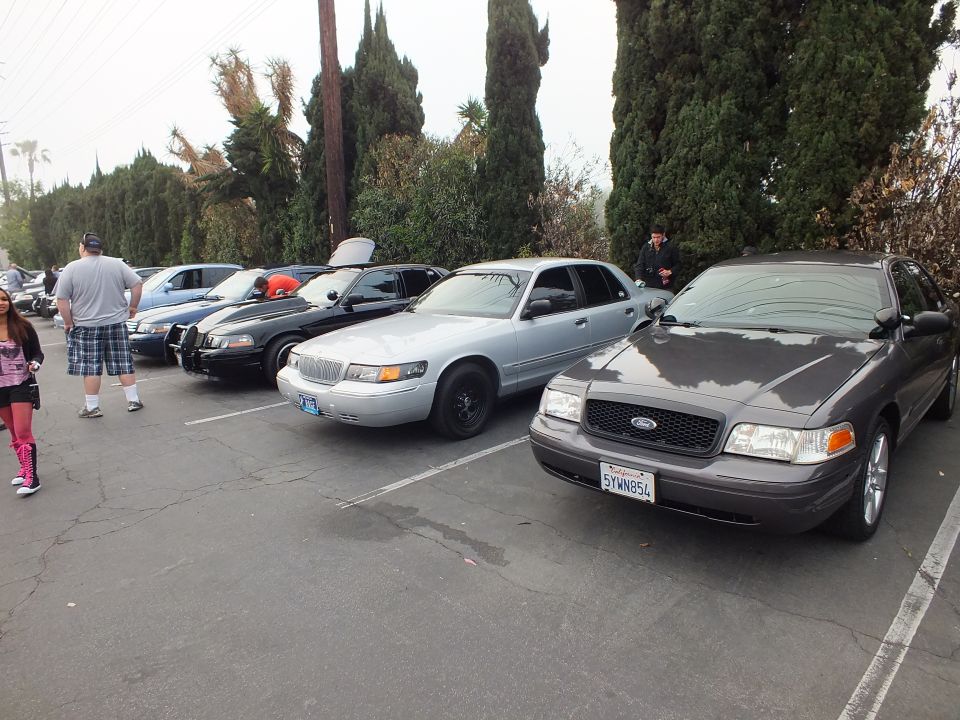 Gray Crown Victoria and silver Mercury Grand Marquis with other sedans and people