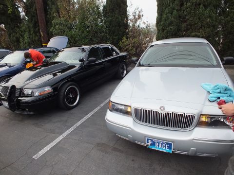 2003 Ford Crown Victoria - Black Ford Crown Victoria with hood up next to silver Mercury Grand Marquis bearing Nevada RAGE plate being detailed
