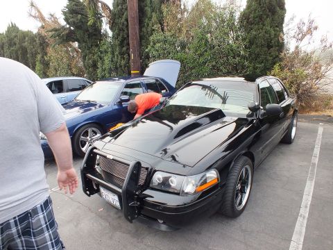 2003 Ford Crown Victoria - Lowered black Ford Crown Victoria fitted with police push bar and black wheels, hood open, at a car meet