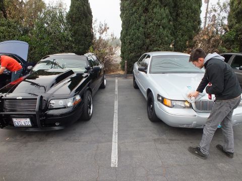 2003 Ford Crown Victoria - Black Ford Crown Victoria with EVILVIC plate and push bar next to a silver Lincoln being detailed by a person