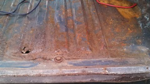 1979 Ford Bronco - The ribbed floor of a truck bed shows significant rust damage and a hole.