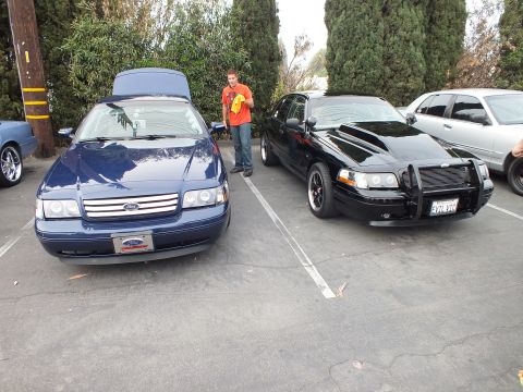 2003 Ford Crown Victoria - Dark blue Ford Crown Victoria beside a black push-bar Crown Victoria, a person with yellow cloth standing between