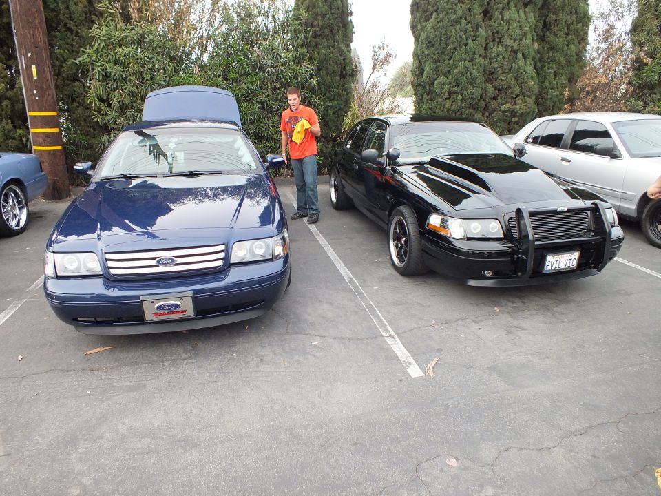 Blue Ford Crown Victoria and black push-bar sedan parked with person holding cloth