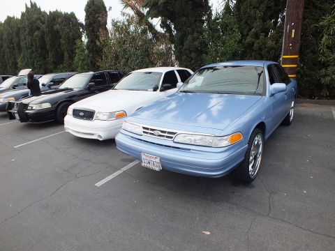 2003 Ford Crown Victoria - Light blue Ford Crown Victoria with chrome wheels beside a white Crown Victoria and a dark police-style sedan