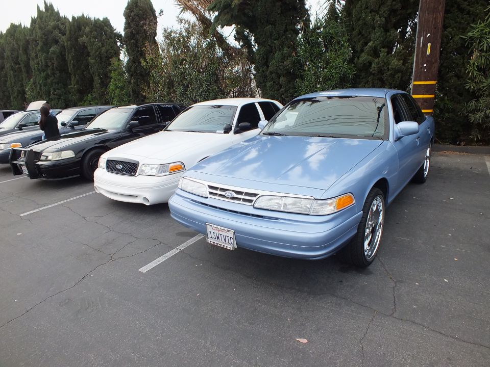Light blue Ford Crown Victoria and white Crown Victoria parked in a lot